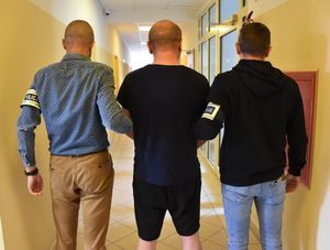 Nieumundurowani policjanci prowadzą zatrzymanego mężczyznę.