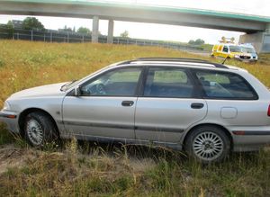 Samochód osobowy na łące. W tle autostrada, pojazd służby drogowej oraz radiowóz