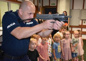 Policjant z bronią. W tle dzieci