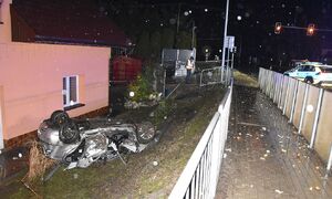 Zdeformowany po dachowaniu pojazd znajduje się na posesji w pobliżu domu. Na jezdni widoczny jest radiowóz, Zdjęcie wykonane nocną porą.