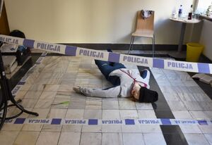 Na podłodze znajduje się manekin, który ogrodzony jest taśmą z napisem Policja
