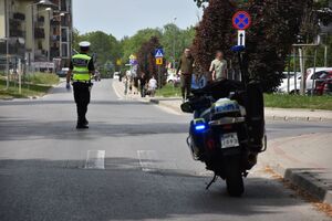 Policjant kieruje ruchem. Na ulicy stoi policyjny motocykl