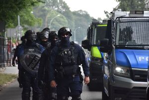 Policjanci zabezpieczający mecz. Obok nich na drodze zaparkowane radiowozy