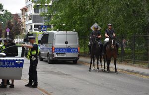 Policyjni jeźdźcy na koniach podczas zabezpieczenia meczu. Po drugiej stronie radiowóz i policjanci
