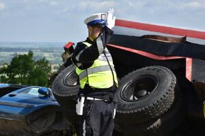 Policjant kieruje ruchem. W tle przewrócona cysterna i samochód ososbowy
