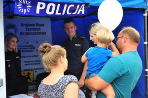 Mężczyzna trzymający dziecko na rękach przy policyjnym stanowisku. Obok kobieta. ma drugim palnie dwie policjantki oraz policjant.