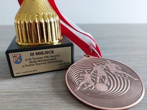 Tabliczka na podstawce pucharu z tytułem, miejscem i datą oraz brązowy medal