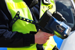 Ręczny miernik prędkości trzymany w ręce przez policjanta w żółtej kamizelce
