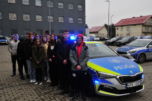 Dzieci stojące na parkingu obok radiowozu, który ma włączone sygnały świetlne