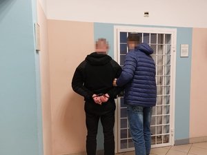 Policjant z zatrzymanym mężczyzną przed kratą aresztu policyjnego