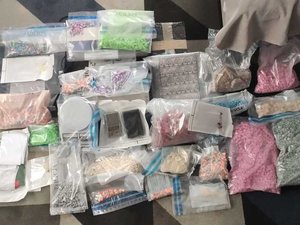 Kilkanaście różnokolorowych narkotyków w formie tabletek oraz wagi ułożone na podłodze