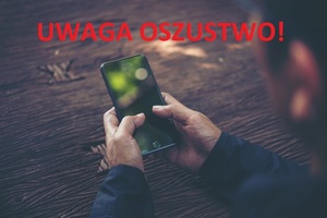 Na zdjęciu widać smartfona trzymanego w rękach. Na górze napis uwaga oszustwo