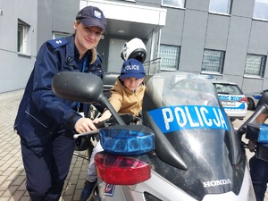 Policjantka oraz chłopiec w czapce z napisem &quot;police&quot; siedzący na motocyklu. Oboje patrzą w obiektyw aparatu