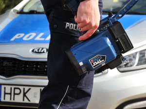 Miernik prędkości w ręce policjanta stojącego na tle radiowozu