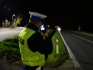 Policjant stojący przy drodze i mierzący w nocy prędkość pojazdów