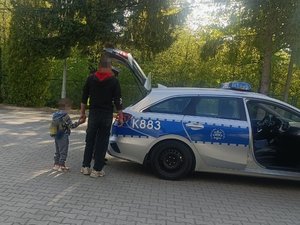 Ojciec trzymający syna za rękę i stojący przy radiowozie