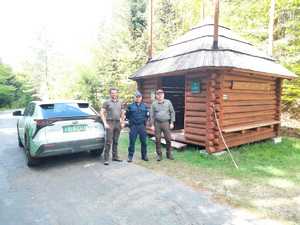 Policjant oraz strażnicy na tle lasu i pojazdów służbowych