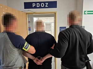 Policjanci z zatrzymanym mężczyzną przed drzwiami policyjnej izby zatrzymań