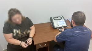 Kobieta w kajdankach, obok alkomat i siedzący policjant