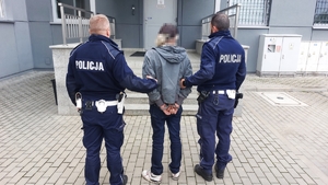 Policjanci trzymający przed komendą mężczyznę w kajdankach