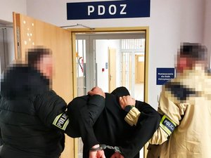 Policjanci kryminalni trzymający mężczyznę w kajdankach przed policyjną izbą zatrzymań