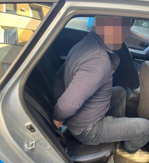 Zatrzymany mężczyzna siedzący skuty w radiowozie