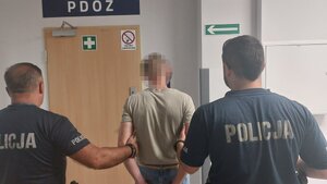 Policjanci z zatrzymanym mężczyzną przed drzwiami PDOZ