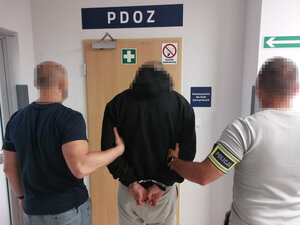 Zatrzymany mężczyzna stojący z policjantami przed PDOZ