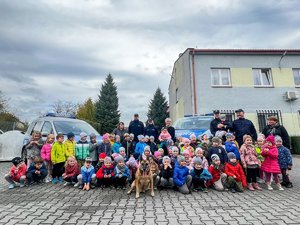 Zdjęcie przedstawie grupę dzieci, opiekunów oraz policjantów stojących przy dwóch radiowozach na zewnątrz. Zdjęcie wykonane na parkingu Komendy Powiatowej Policji w Leżajsku.