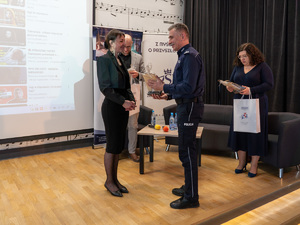 Zdjęcia przedstawiają przebieg debaty. Na zdjęciach widoczni są umundurowani policjanci oraz prelegenci. Debata społeczna odbyła się w Zespole Szkół Licealnych im. Bolesława Chrobrego. Na wybranych kadrach widoczna jest tłumnie zgromadzona na sali koncertowej młodzież.