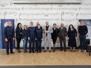 Zdjęcia przedstawiają przebieg debaty. Na zdjęciach widoczni są umundurowani policjanci oraz prelegenci. Debata społeczna odbyła się w Zespole Szkół Licealnych im. Bolesława Chrobrego. Na wybranych kadrach widoczna jest tłumnie zgromadzona na sali koncertowej młodzież.