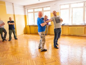 Zdjęcia przedstawiają osoby biorące udział w szkoleniu z samoobrony. Zdjęcia są na sali gimnastycznej.