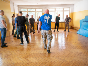 Zdjęcia przedstawiają osoby biorące udział w szkoleniu z samoobrony. Zdjęcia są na sali gimnastycznej.