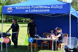 Na zdjęciu dwóch policjantów i policjantka w umundurowaniu służbowym, przebywający wraz z uczestnikami w niebieskim namiocie z napisem &#039;Komenda Powiatowa Policji w Lubaczowie.