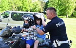 Na zdjęciu policjant w umundurowaniu służbowym i dwójka dzieci siedząca na quadzie.