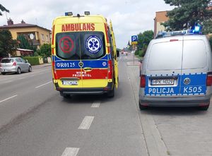 Zdjęcie przedstawia karetkę i oznakowany radiowóz policyjne stojące na drodze.