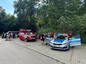 Na zdjęciu stoją dwa zaparkowane pojazdy straży pożarnej i policji. Uczestnicy wydarzenia je oglądają.