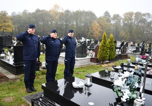 Na cmentarzu Komendant Powiatowy Policji w Lubaczowie oraz przedstawiciele kadry kierowniczej oddają hołd. W tle groby. Policjanci występują w umundurowaniu służbowym.