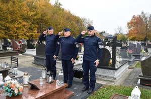 Na cmentarzu Komendant Powiatowy Policji w Lubaczowie oraz przedstawiciele kadry kierowniczej oddają hołd. W tle groby. Policjanci występują w umundurowaniu służbowym.