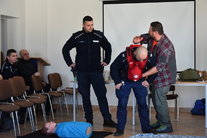 Dwóch policjantów w umundurowaniu służbowym i mężczyzna ćwiczą.