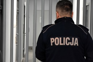 Policjant w umundurowaniu służbowym i kraty.