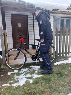 policjant stoi przy domu z rowerem z kokardą