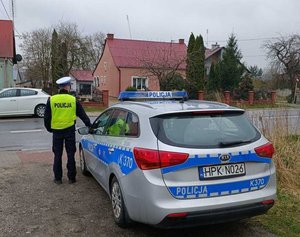 policjant stoi przy radiowozie przy drodze