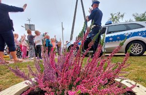 policjanci stoją przy radiowozie przed nimi na placu zabaw grupa dzieci