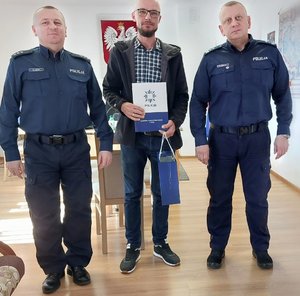 mężczyzna stoi pomiędzy policjantami w ręku trzyma torbę prezentową i teczkę z napisem policja komenda powiatowa policji w nisku