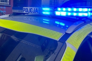 policyjna belka radiowozu z włączonymi światłami błyskowymi koloru niebieskiego i napis policja