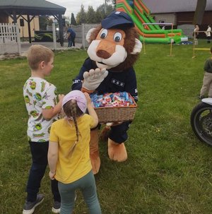 policyjna maskotka lew podczas pikniku rodzinnego rozdaje słodycze obok dwoje dzieci