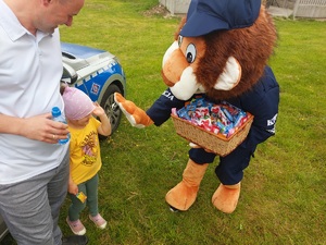 policyjna maskotka lew rozdaje najmłodszym słodycze podczas pikniku rodzinnego w plenerze