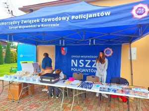 niebieski namiot z napisem samorządny związek zawodowy policjantów pod którym jest stolik na nim ułożone smycze długopisy oraz ulotki