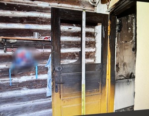 wnętrze domu po pożarze, widok nadpalonych drzwi przy których ustawiona jest miarka
